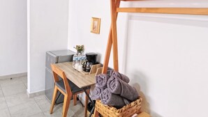 Una kitchenette pequeña con refrigerador, cafetera y pileta. Hay una mesa de madera con una silla y una cesta de toallas dobladas.
