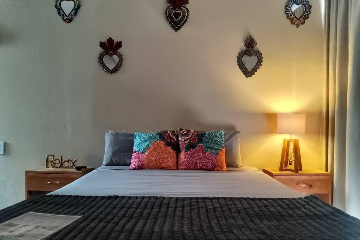 A bed with patterned pillows, a bedside table with a lamp, and heart-shaped wall decorations.