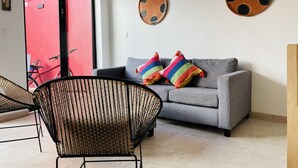 Un salón con un sofá gris, almohadas coloridas, una silla negra y dos adornos en la pared.