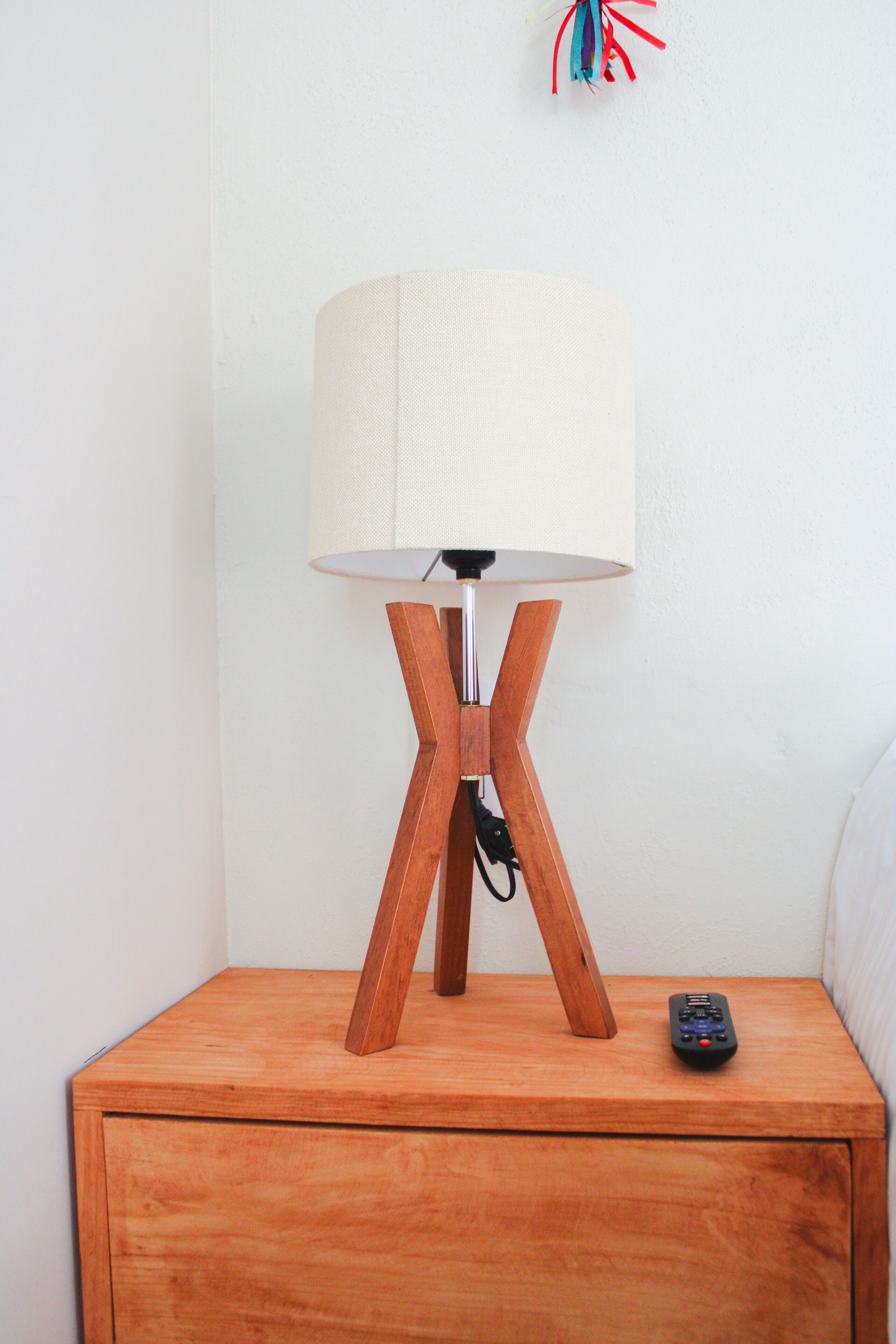 Une table de chevet en bois, avec une lampe et une télécommande.