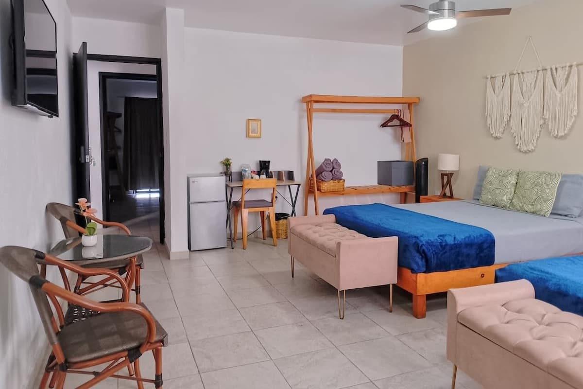 A room with two beds, a desk, a chair, a small table, and a ceiling fan.