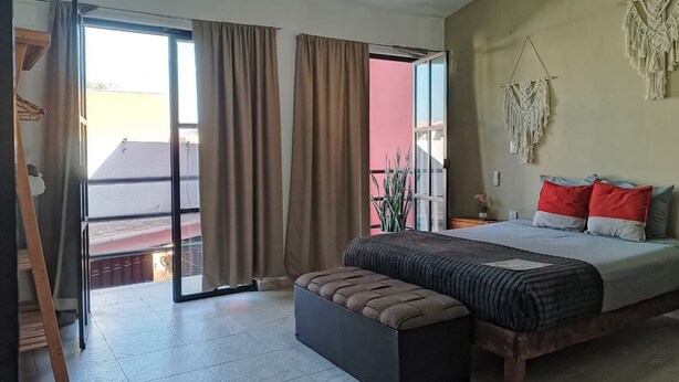 Un dormitorio con cama, un banco, una puerta corrediza de vidrio y un tapiz de macramé en la pared.