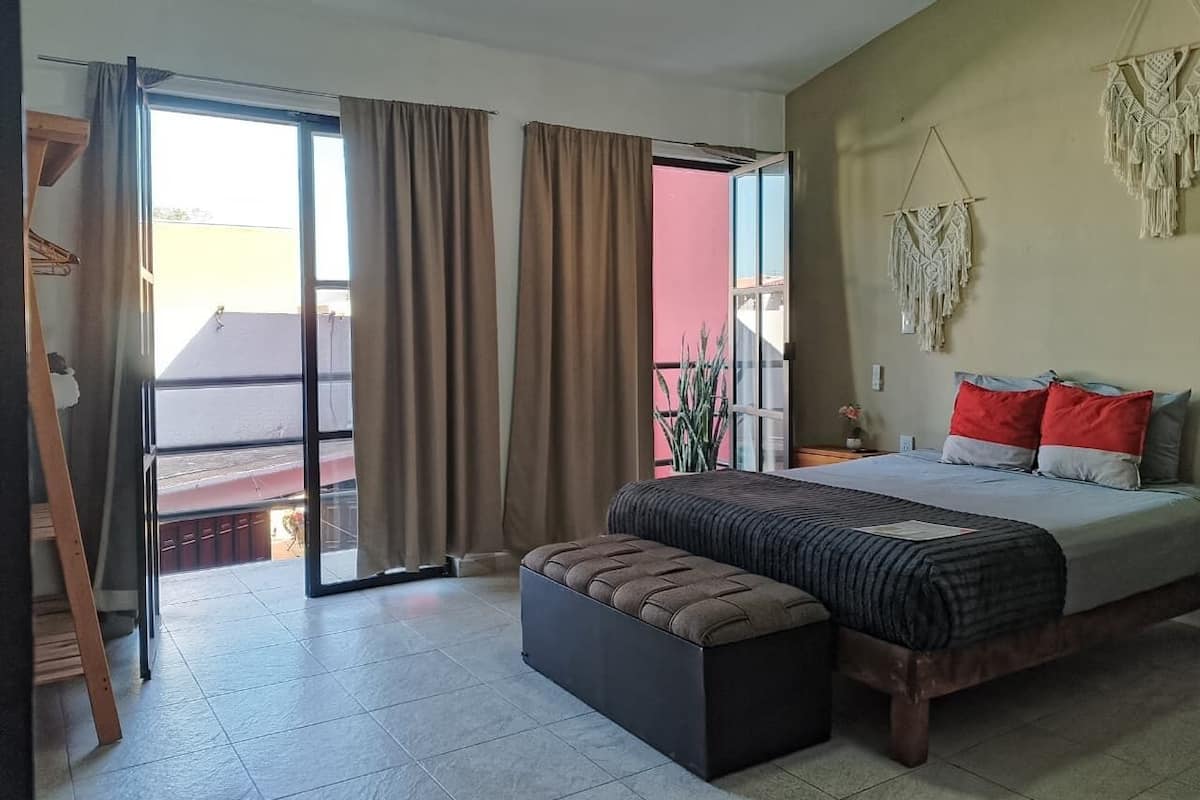 A bedroom with a bed, a bench, a sliding glass door, and a macrame wall hanging.