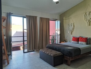 Un dormitorio con cama, un banco, una puerta corrediza de vidrio y un tapiz de macramé en la pared.