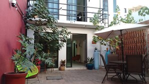 Un patio con plantas en macetas, un comedor con sillas y una mesa, y un edificio con un balcón.