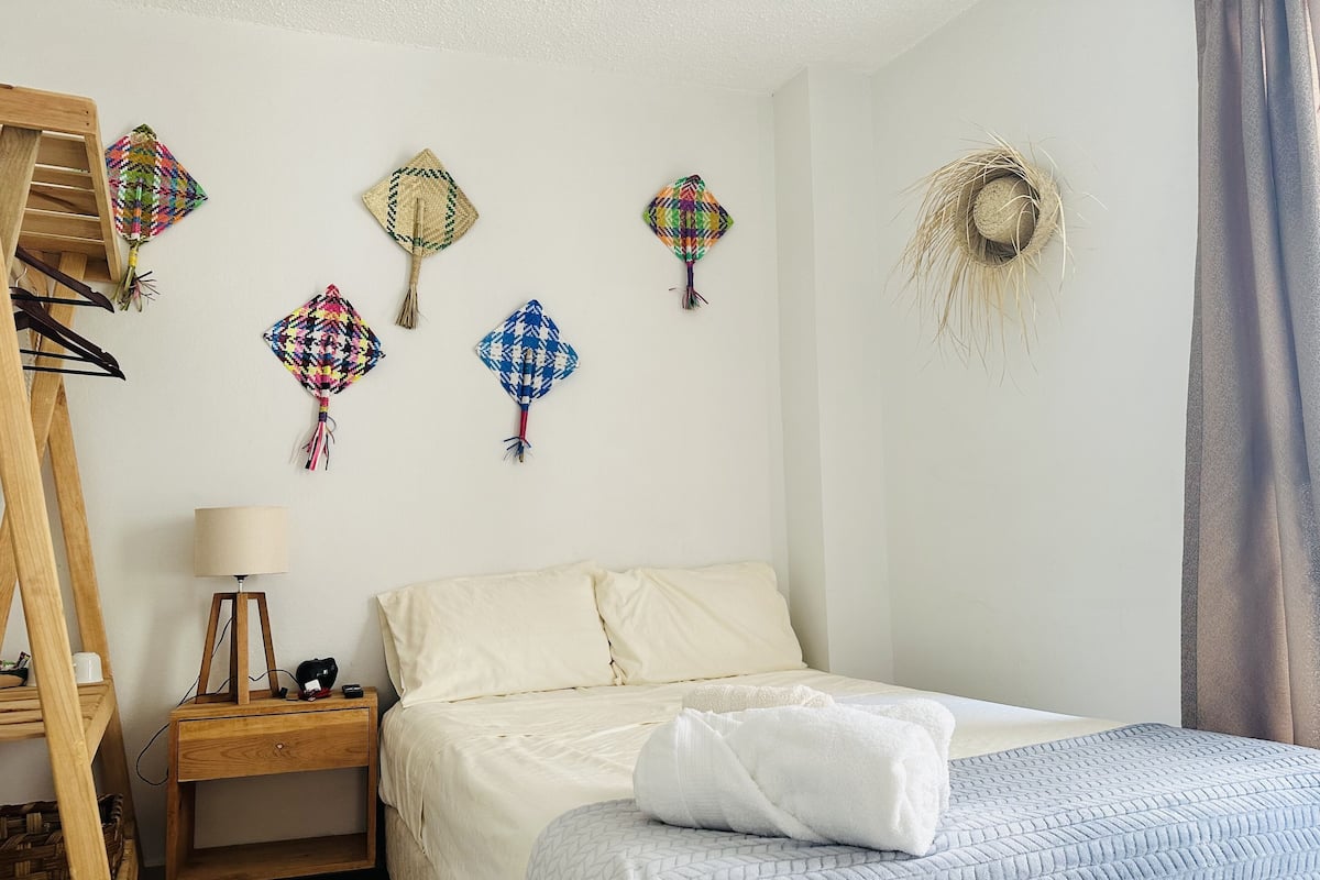 A bedroom with a bed, a nightstand, a lamp, and several kites hanging on the wall.