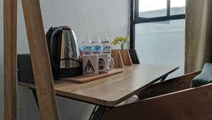 Una mesa de madera con una tetera, botellas de agua y tazas, una planta pequeña y una ventana con vistas.