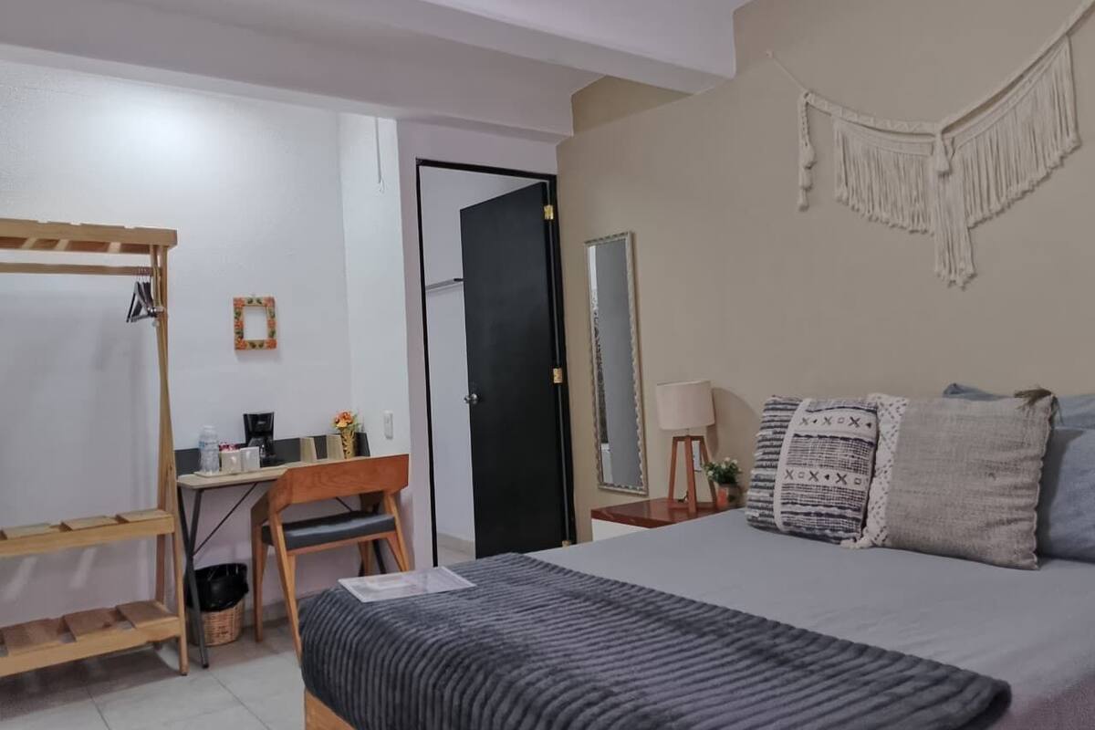 A bedroom with a bed, a desk, a chair, a wardrobe, and a mirror.