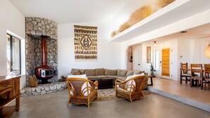 Un salon moderne avec une cheminée en pierre, une grande tapisserie tissée et un coin repas avec des meubles en bois.