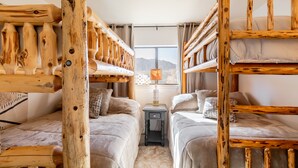 Une chambre avec deux lits, des têtes de lit en bois, une table de chevet, une lampe et une vue sur les montagnes par la fenêtre.