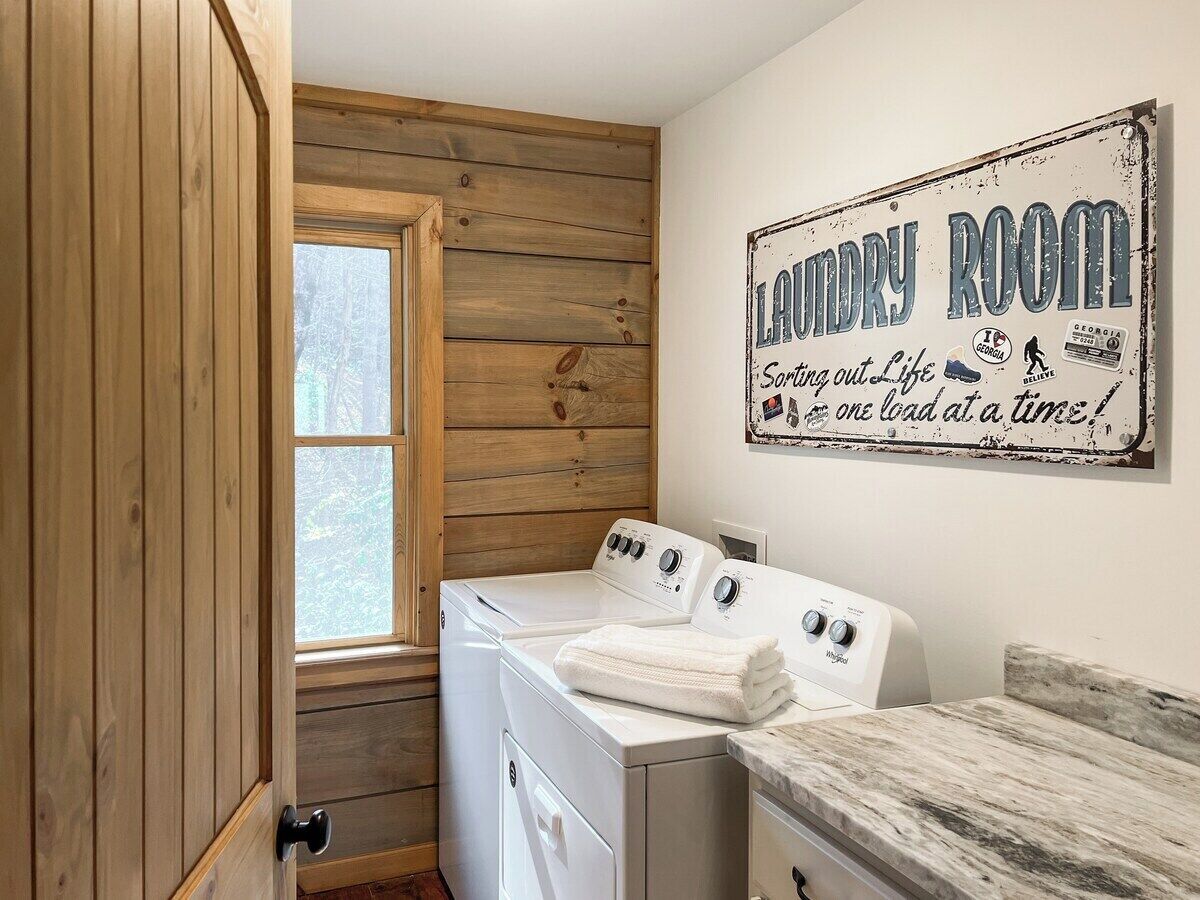 Un lavadero con paredes de madera, un ventanal grande y un cartel que dice: 'Laundry Room Sorting out Life one load at a time'.