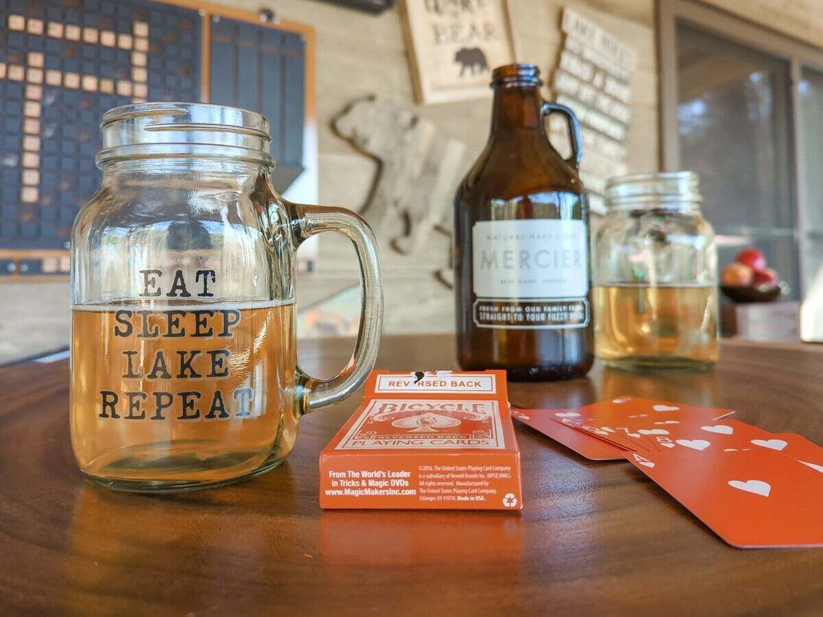 Een tafel met een glazen pot met de tekst 'EAT SLEEP LAKE REPEAT', een biertje, een pak Bicycle Playing Cards en speelkaarten.