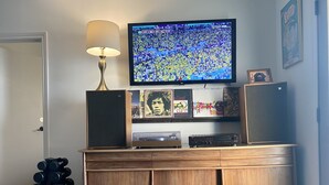 Ett vardagsrum med en tv-apparat som visar en sportevenemang, en lampa, högtalare och ett träskåp med diverse föremål.