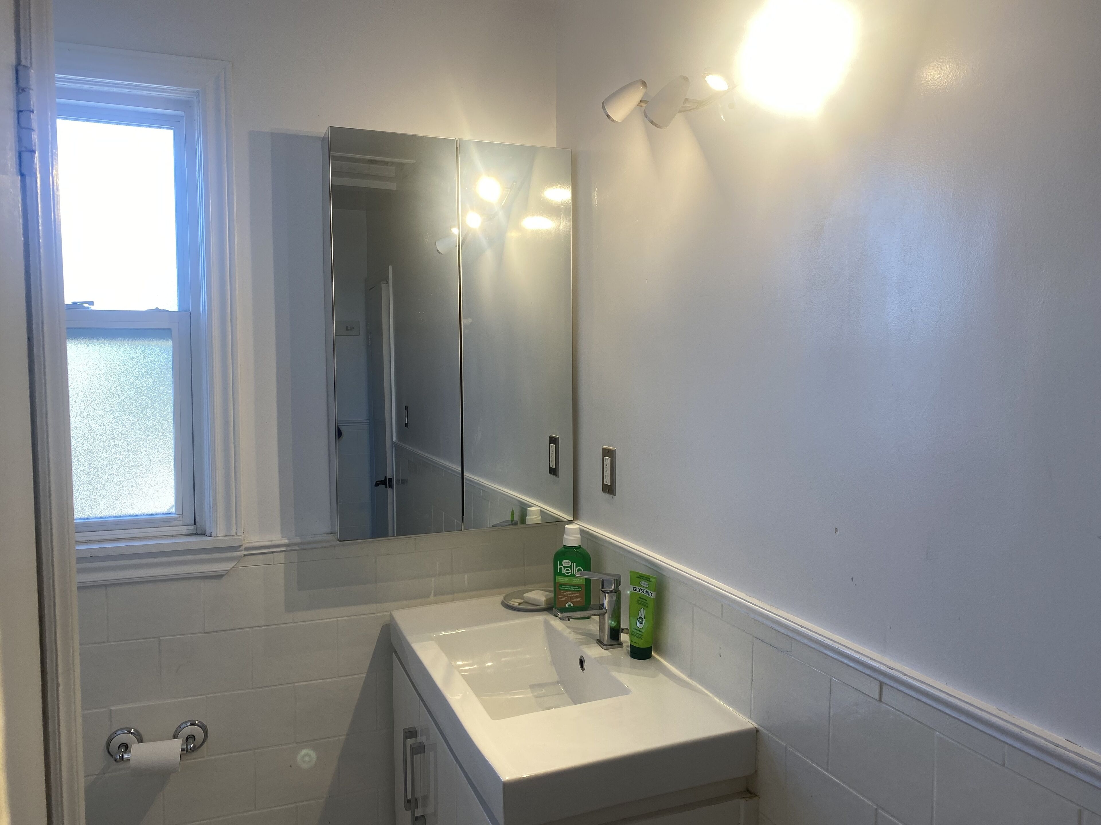 A bathroom with a white sink, a mirror, and a window.