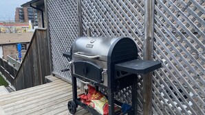 En portabel grill med ett underrede, placerad på ett trädäck intill ett spaljé.