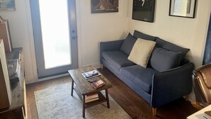 Ett vardagsrum med en mörkblå soffa, ett soffbord i trä och en dörr med ett glasparti.
