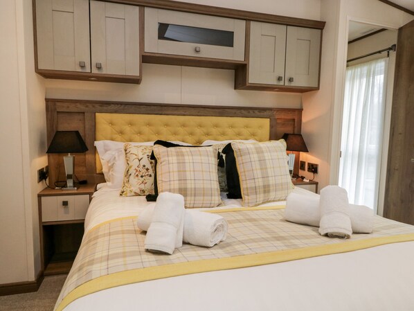 A neatly made bed with a yellow headboard, two bedside tables with lamps, and a television above the bed.
