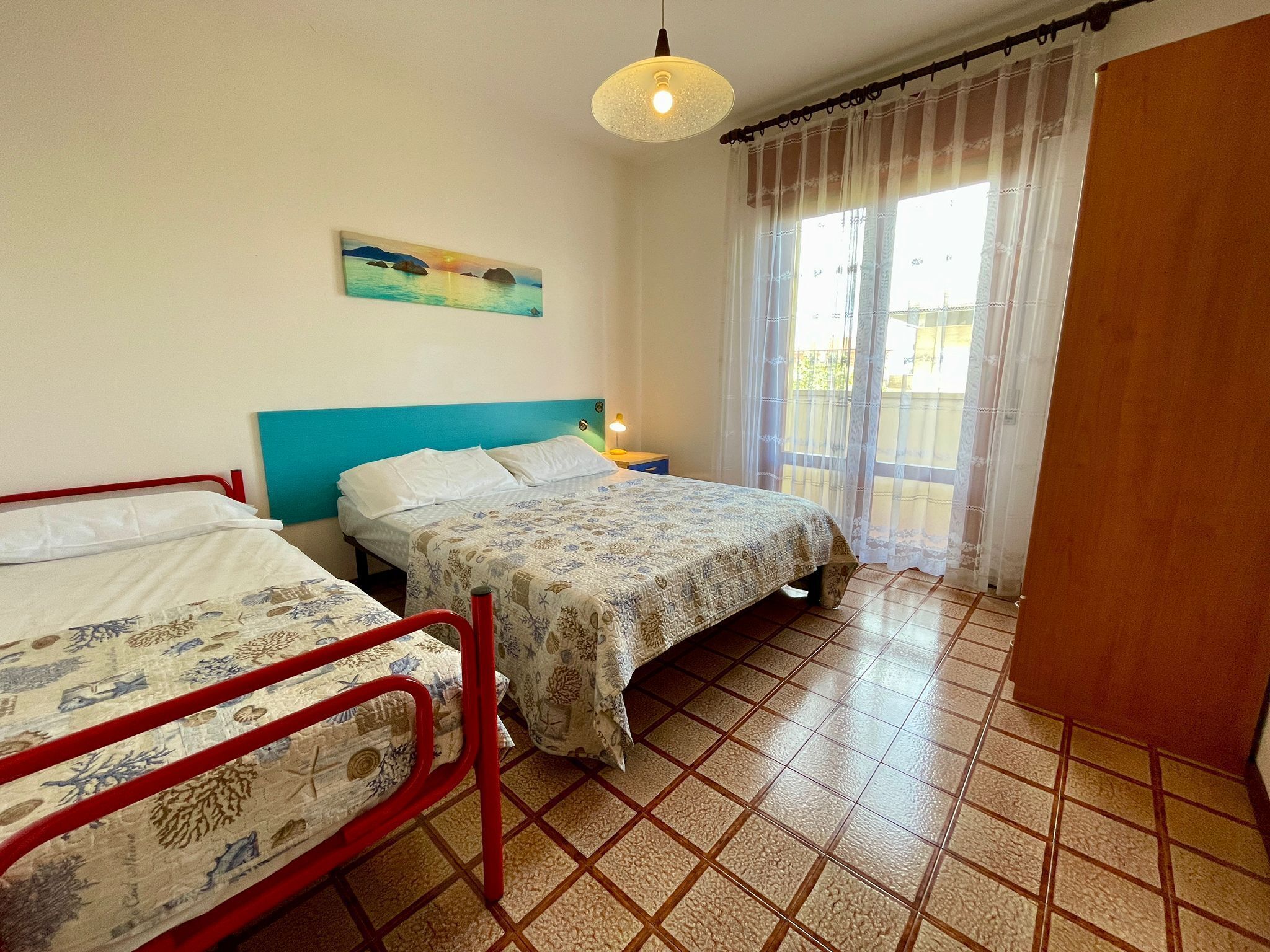 A bedroom with two beds, a window with curtains, a painting on the wall, and a tiled floor.