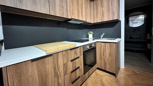 A modern kitchen with wooden cabinets, a white countertop, a built-in oven, and a black backsplash. - Maisonette Near Beach & City Center (Heraklion)