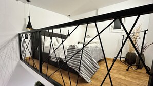 A bedroom with a bed, a bedside table, a hanging light, and a window. - Maisonette Near Beach & City Center (Heraklion)