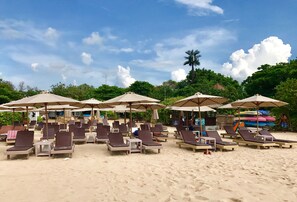 Relax on comfortable sun loungers under shaded umbrellas on the sandy beach.