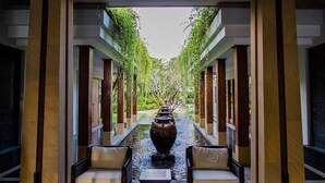 A corridor with a water feature, two chairs, and a view of a garden.