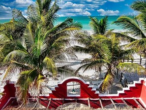 Ein Strand mit Palmen, einem roten Zaun und blauem Himmel.