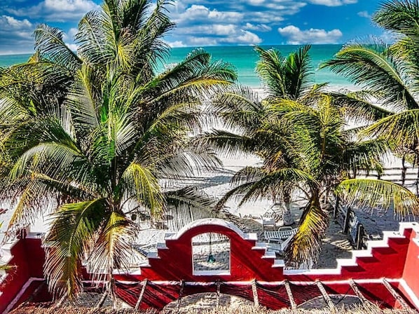A beach with palm trees, a red fence, and a clear blue sky.