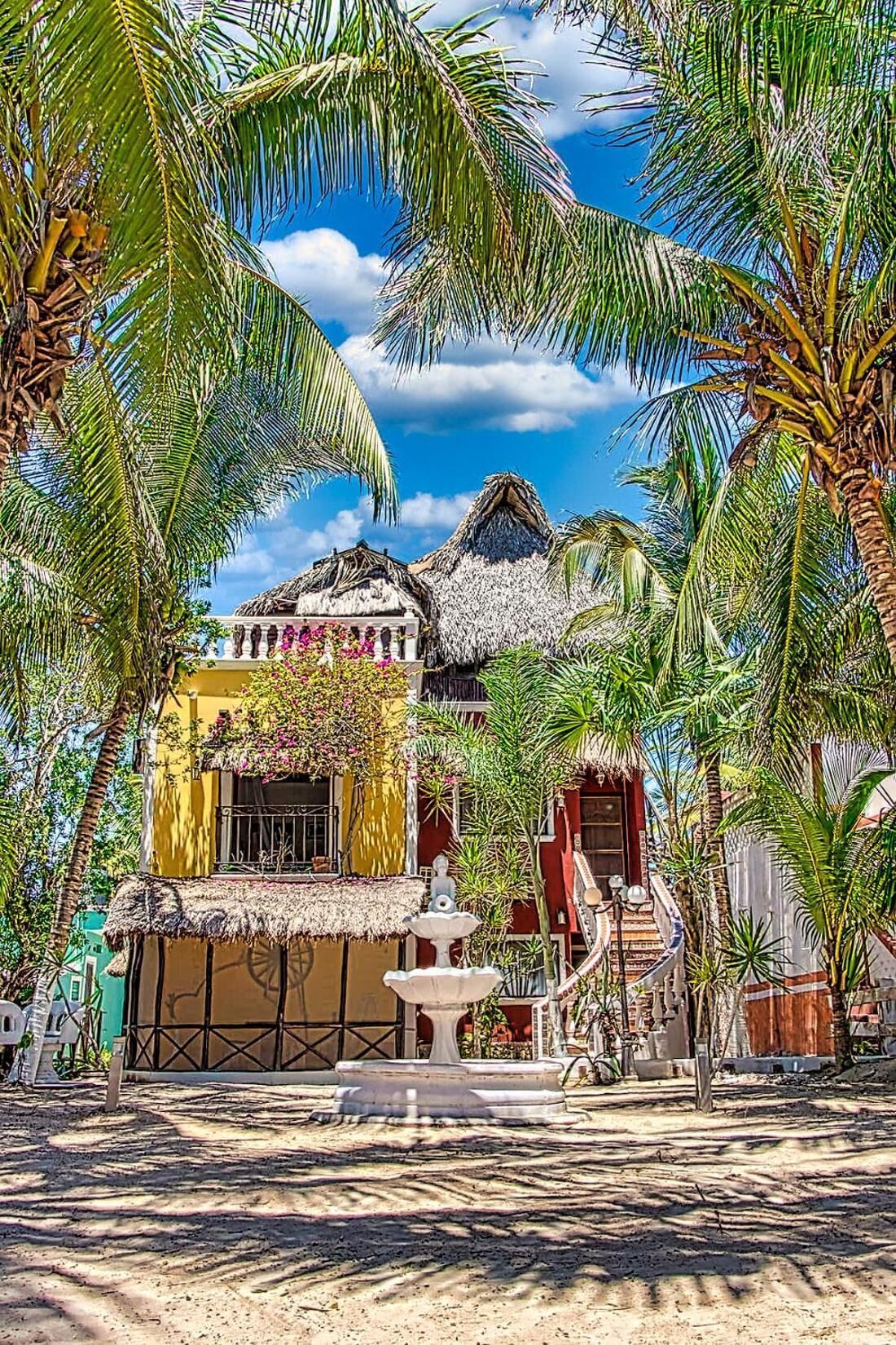 Un resort tropical con edificios de techo de paja, palmeras y un cielo azul claro.