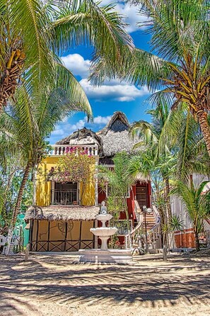 A tropical resort with thatched-roof buildings, palm trees, and a clear blue sky.