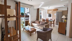 Una sala moderna con sofá, una mesita de centro y comedor. Se observa una cocina con refrigerador y armarios.