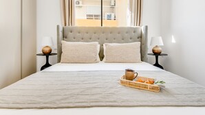 Una cama bien hecha con un edredón gris, dos almohadas y una bandeja con una taza y croissants.
