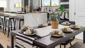 A modern kitchen with a dining area, featuring a marble countertop, a woven basket with a plant, and neatly arranged plates of food. - Group-Friendly Home | Patio & Parking for 5 (Miami)