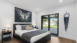 A bedroom with a large bed, two bedside tables, a nightstand, a wall-mounted mirror, and a butterfly painting. - Group-Friendly Home | Patio & Parking for 5 (Miami)