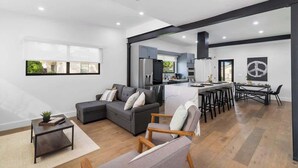 A modern living room with a grey sectional sofa, a small coffee table, and a dining area with a bar stool and a table. - Group-Friendly Home | Patio & Parking for 5 (Miami)