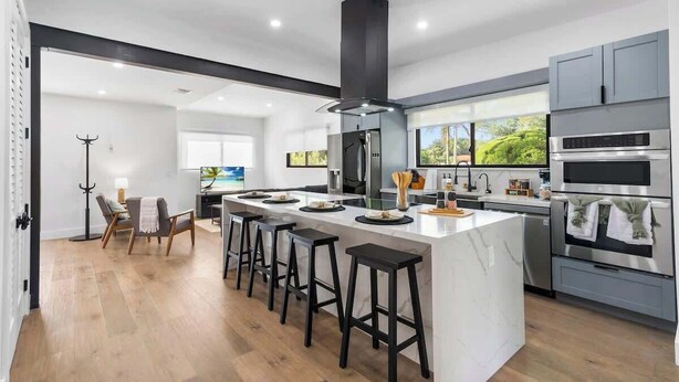 A modern kitchen with a central island, bar stools, a built-in oven, and a large window. - Group-Friendly Home | Patio & Parking for 5 (Miami)
