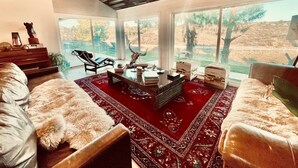 A spacious living room with a red carpet, leather sofas, a coffee table, and a large window offering a view of the outdoors. - Love Casa Pool Fire Pit Close To Wineries (Temecula)
