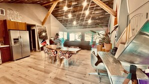 A spacious kitchen with a modern refrigerator, wooden dining table with patterned chairs, and a large window providing natural light. - Love Casa Pool Fire Pit Close To Wineries (Temecula)