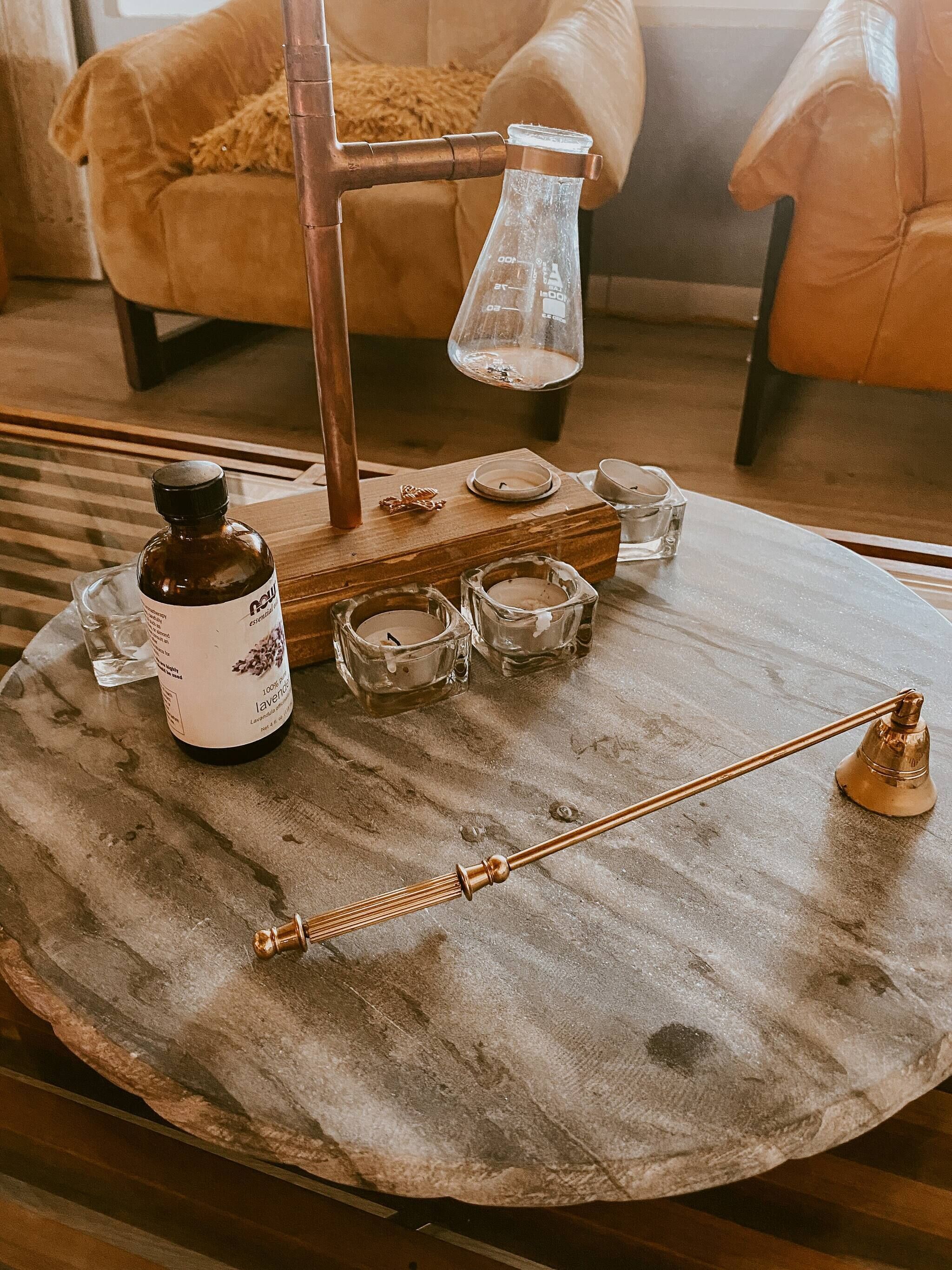 Une table en bois sur laquelle se trouvent une bouteille d’huile essentielle de lavande, un chandelier en métal et plusieurs récipients en verre.