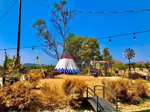 A rustic outdoor setting with a conical structure, possibly a tipi, surrounded by dry vegetation and a windmill. - Love Casa Pool Fire Pit Close To Wineries (Temecula)