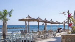 A beachside café with outdoor seating, umbrellas, and a view of the sea. - Sanders Crystal 2 - Cute 1-bdr Apt With Shared Rooftop (Limassol)