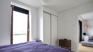 A bedroom with a large bed, a wardrobe, a small table, and a view of a balcony. - Modern Apartment in Copenhagen Sluseholmen With a Marvellous View (Copenhagen)