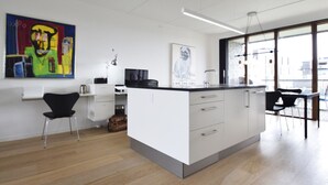 A modern kitchen with a central island, white cabinetry, and a large window providing natural light. - Modern Apartment in Copenhagen Sluseholmen With a Marvellous View (Copenhagen)