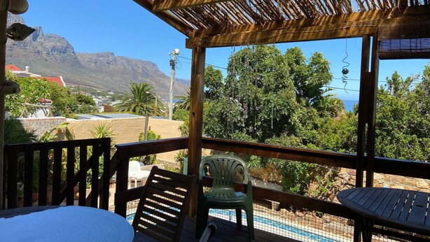 A covered outdoor area with a pool, wooden deck, and chairs. - Room-living In Camps Bay Blue (Cape Town)