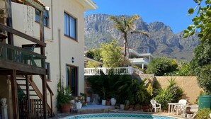 A swimming pool with a stone border, surrounded by a patio area with chairs and potted plants. - Room-living In Camps Bay Blue (Cape Town)