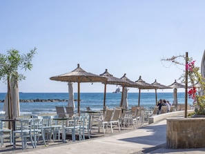 A beachside café with outdoor seating, umbrellas, and a view of the sea. - Sanders Crystal 2 - Penthous With Shared Rooftop (Limassol)