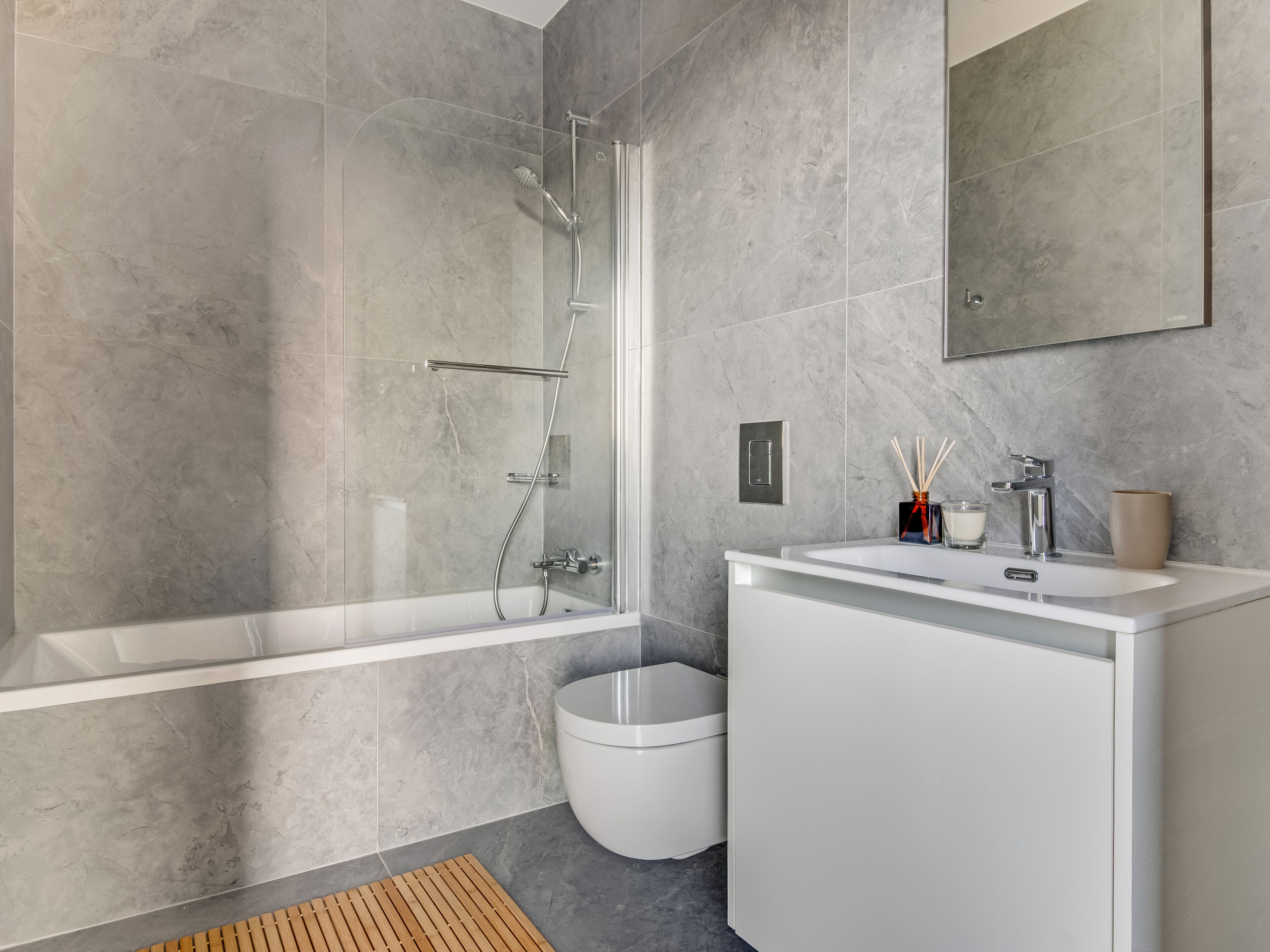 Un baño moderno con ducha envuelta en vidrio, tocador blanco y pared con mosaicos de mármol.