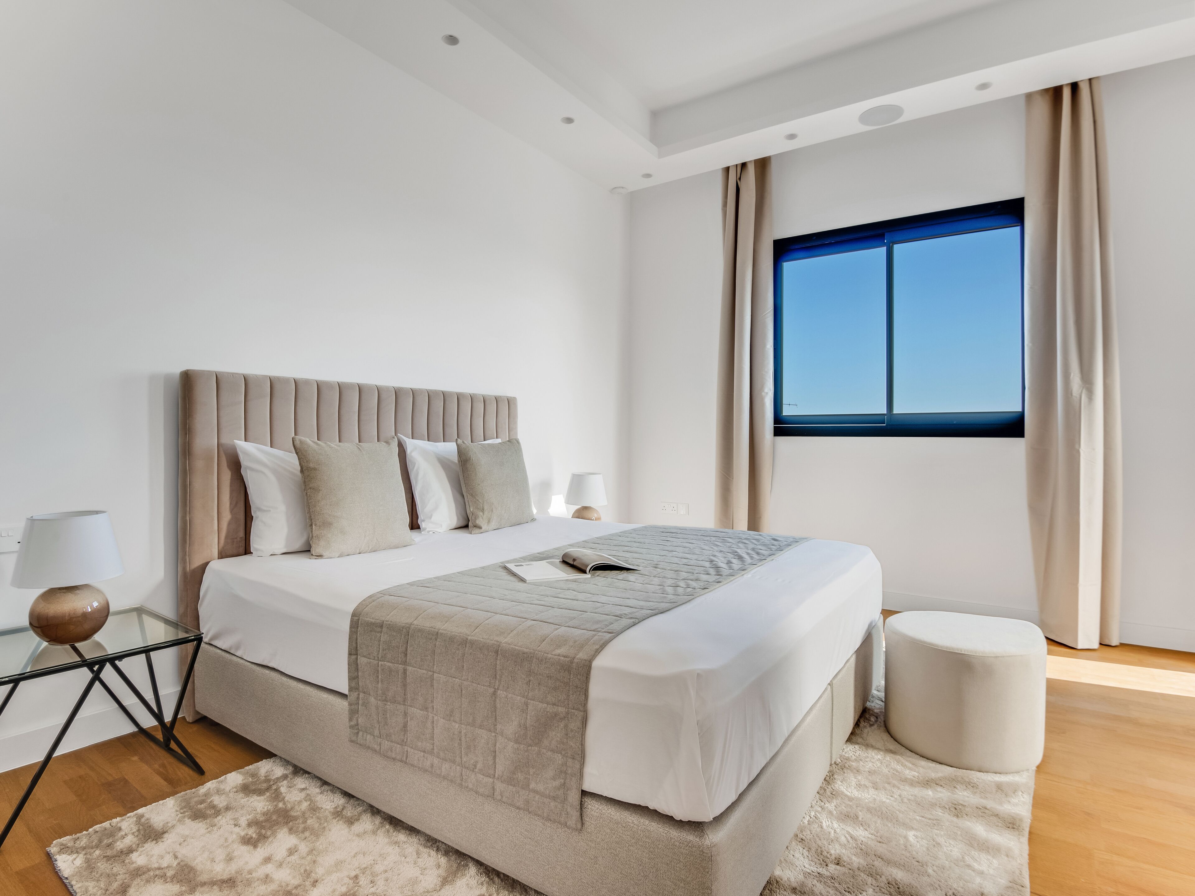 A modern bedroom with a large bed, a bedside table, a lamp, and a window with curtains.