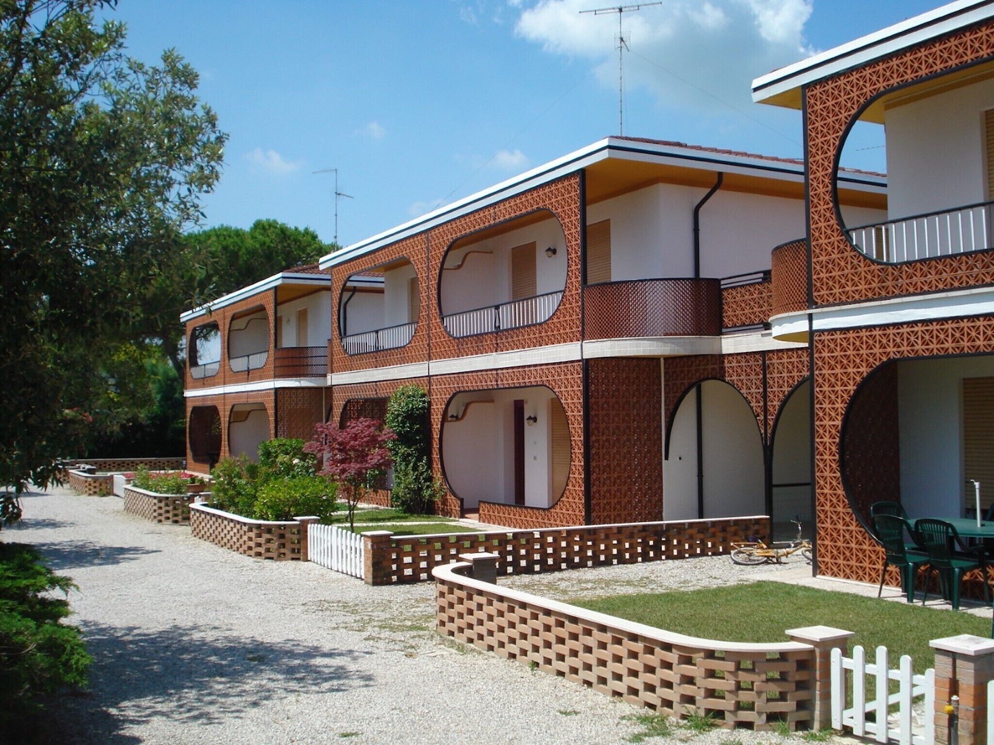 A row of two-story buildings with balconies, a gravel driveway, and a small garden area.