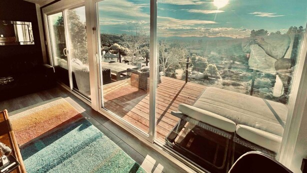 Una habitación con grandes puertas correderas de vidrio que dan a una terraza con vistas a un pueblo y colinas.